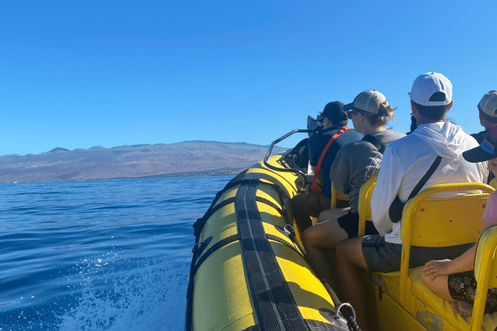 People riding on a yellow inflatable boat on clear blue water.